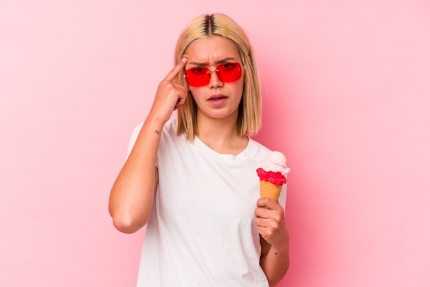 Young venezuelan woman eating an ice cream isolated on pink wall showing a disappointment gesture with forefinger