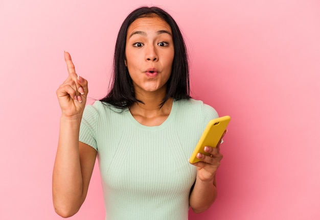 Young Venezuelan woman holding a mobile phone isolated on pink background having an idea, inspiration concept.