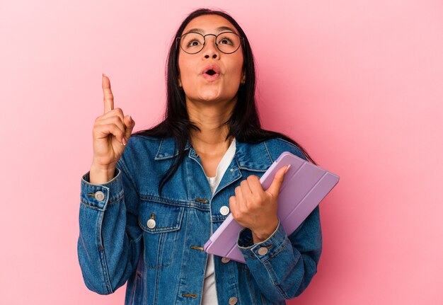 Young venezuelan woman holding a tablet isolated on pink background pointing upside with opened mouth.