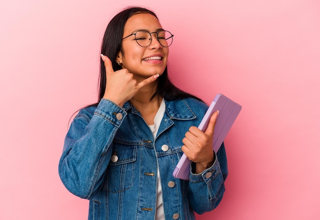 Young venezuelan woman holding a tablet isolated on pink background showing a mobile phone call gesture with fingers