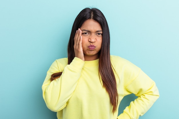 Young Venezuelan woman isolated on blue background blows cheeks, has tired expression. Facial expression concept.