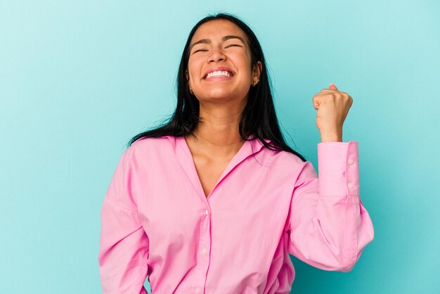 勝利の情熱と熱意の幸せな表現を祝う青い背景に分離された若いベネズエラの女性