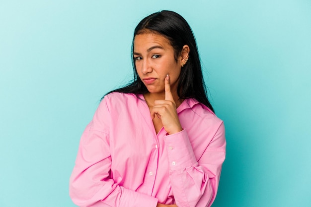 Young Venezuelan woman isolated on blue background contemplating planning a strategy thinking about the way of a business