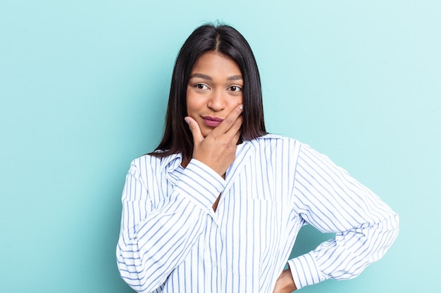 Young Venezuelan woman isolated on blue background covering mouth with hands looking worried.