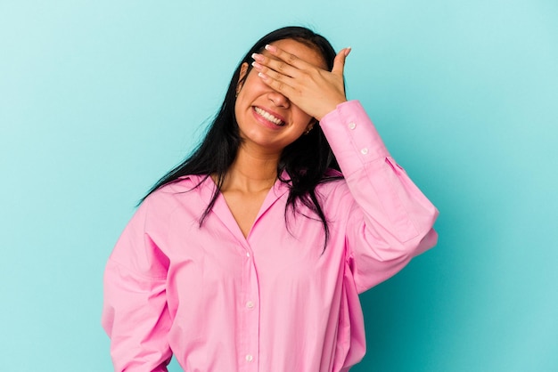 Young Venezuelan woman isolated on blue background covers eyes with hands smiles broadly waiting for a surprise