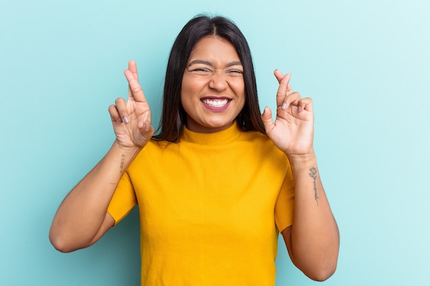 Young Venezuelan woman isolated on blue background crossing fingers for having luck