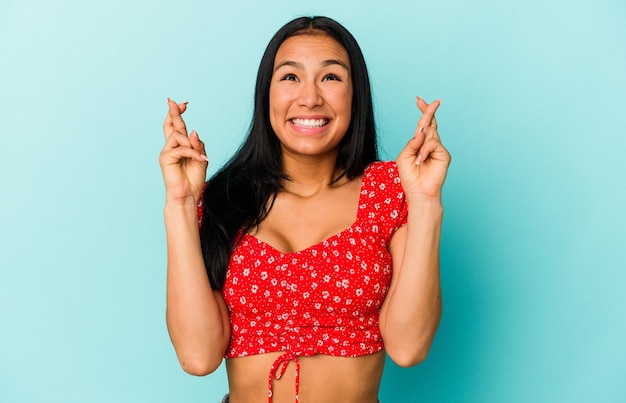 Young Venezuelan woman isolated on blue background crossing fingers for having luck