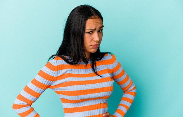 Young Venezuelan woman isolated on blue background frowning face in displeasure keeps arms folded