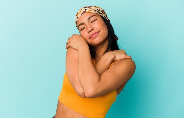 Young Venezuelan woman isolated on blue background hugs, smiling carefree and happy.