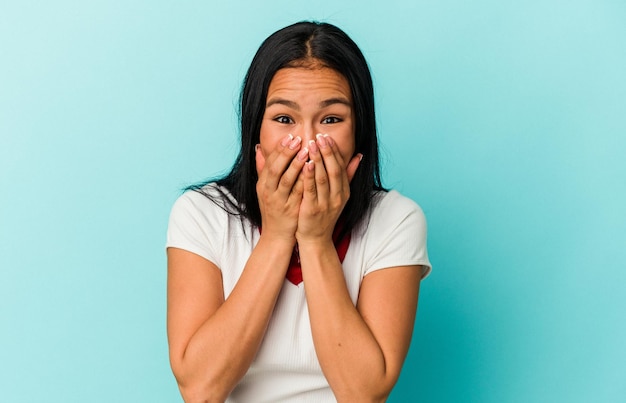 Young Venezuelan woman isolated on blue background laughing about something covering mouth with hands