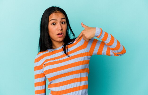 Young Venezuelan woman isolated on blue background person pointing by hand to a shirt copy space, proud and confident