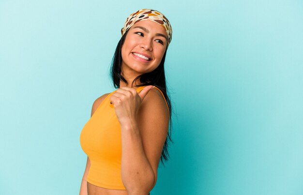 Young Venezuelan woman isolated on blue background points with thumb finger away, laughing and carefree.