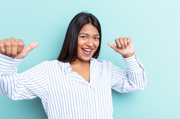 Young Venezuelan woman isolated on blue background raising both thumbs up, smiling and confident.