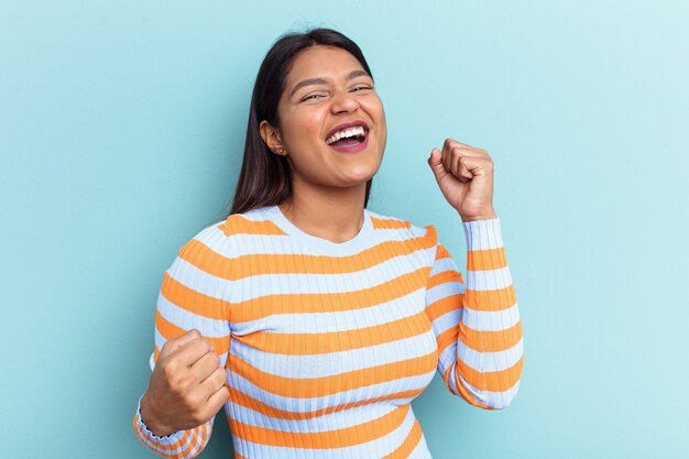 Young Venezuelan woman isolated on blue background raising fist after a victory, winner concept.