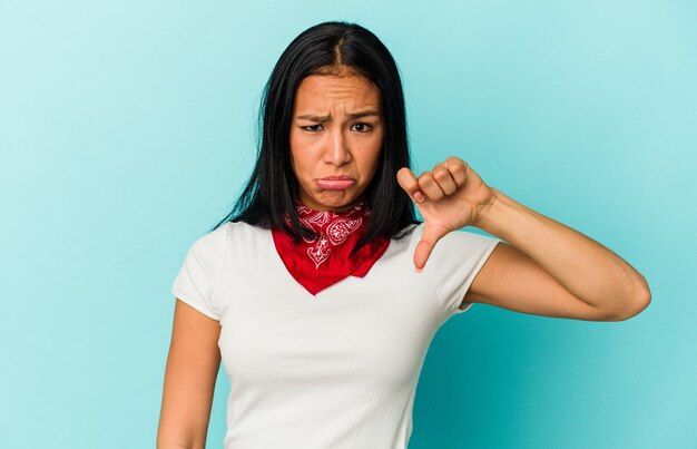 Young Venezuelan woman isolated on blue background showing thumb down, disappointment concept.