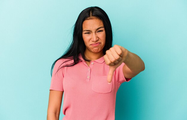 Young Venezuelan woman isolated on blue background showing thumb down and expressing dislike