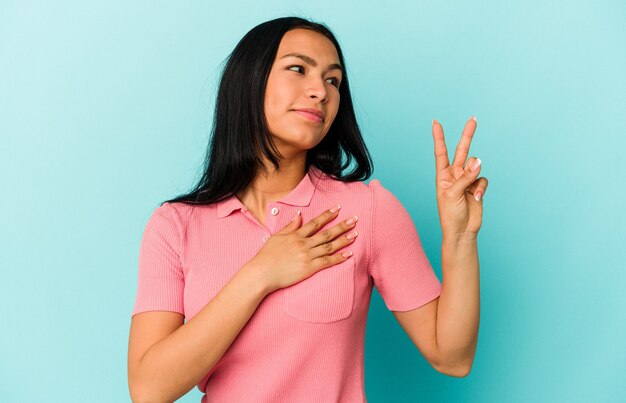 Young Venezuelan woman isolated on blue background taking an oath, putting hand on chest.