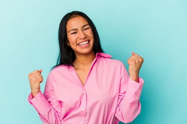 Young Venezuelan woman isolated on blue wall cheering carefree and excited. Victory concept.