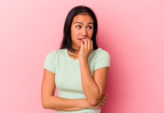 Young Venezuelan woman isolated on pink background biting fingernails, nervous and very anxious.