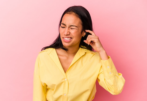 Young Venezuelan woman isolated on pink background covering ears with fingers, stressed and desperate by a loudly ambient.