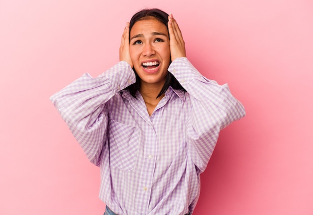 Young Venezuelan woman isolated on pink background covering ears with hands trying not to hear too loud sound.