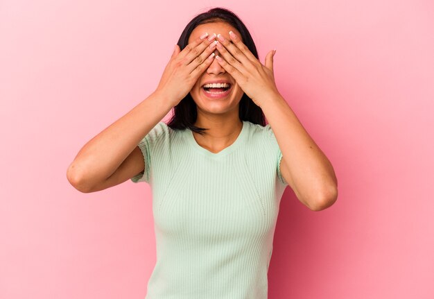 Young Venezuelan woman isolated on pink background covers eyes with hands, smiles broadly waiting for a surprise.