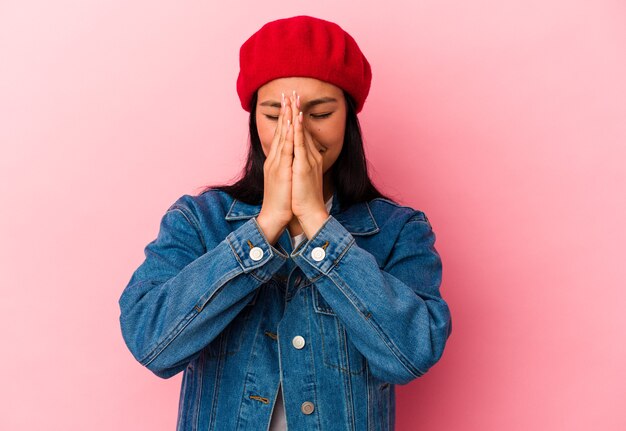 Young Venezuelan woman isolated on pink background holding hands in pray near mouth, feels confident.