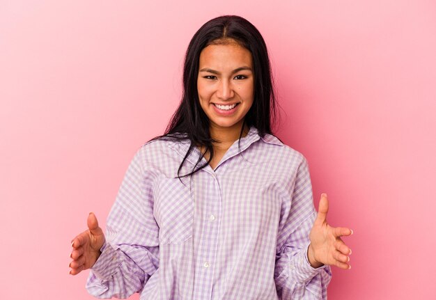 Young Venezuelan woman isolated on pink background holding something with both hands product presentation