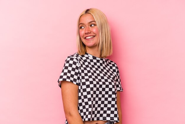 Young venezuelan woman isolated on pink background looks aside smiling, cheerful and pleasant.