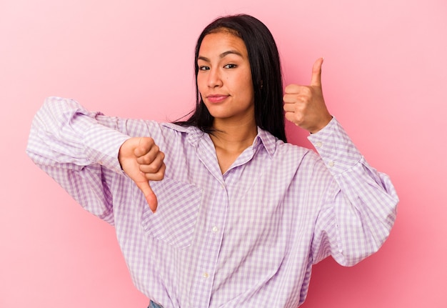 Young Venezuelan woman isolated on pink background showing thumbs up and thumbs down, difficult choose concept