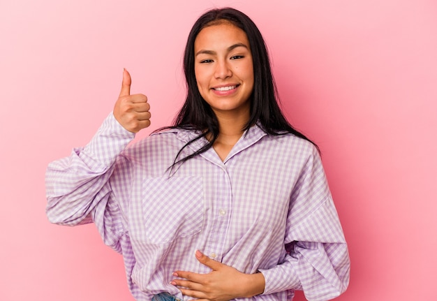 Young Venezuelan woman isolated on pink background touches tummy, smiles gently, eating and satisfaction concept.