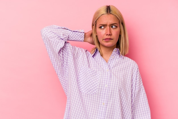 Young venezuelan woman isolated on pink background touching back of head, thinking and making a choice.