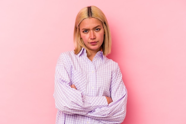 Young venezuelan woman isolated on pink wall frowning face in displeasure, keeps arms folded