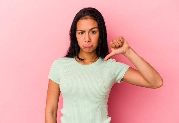 Young Venezuelan woman isolated on pink wall showing a dislike gesture, thumbs down. Disagreement concept.