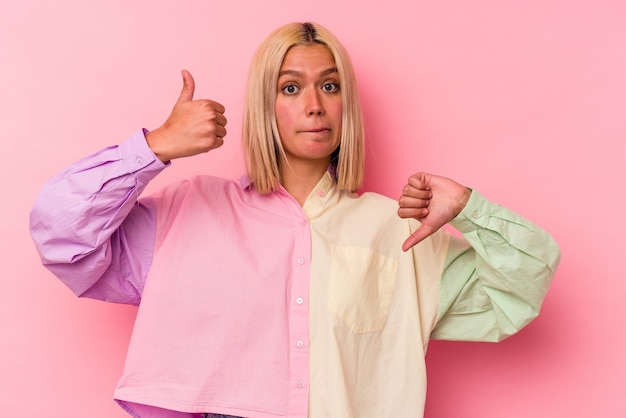 Young venezuelan woman isolated on pink wall showing thumbs up and thumbs down