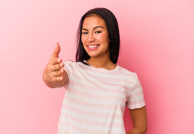 Young Venezuelan woman isolated on pink wall stretching hand in greeting gesture.