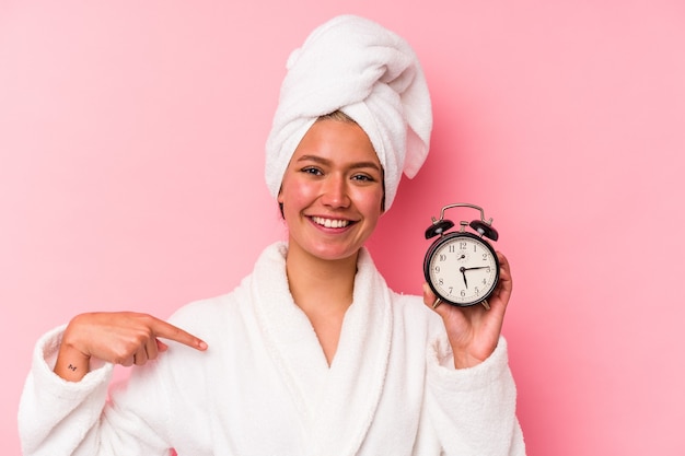 Young venezuelan woman late for work isolated on pink wall person pointing by hand to a shirt copy space, proud and confident