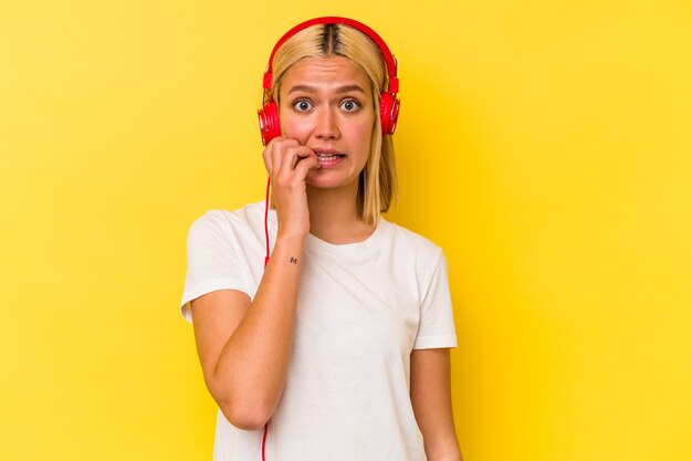 Young venezuelan woman listening music isolated on yellow background biting fingernails, nervous and very anxious.