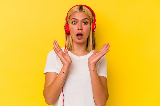 Young venezuelan woman listening music isolated on yellow wall surprised and shocked