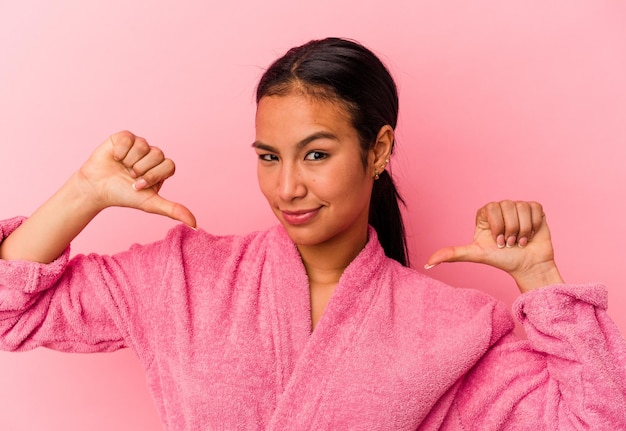 Young Venezuelan woman wearing a bathrobe isolated on pink background feels proud and self confident example to follow