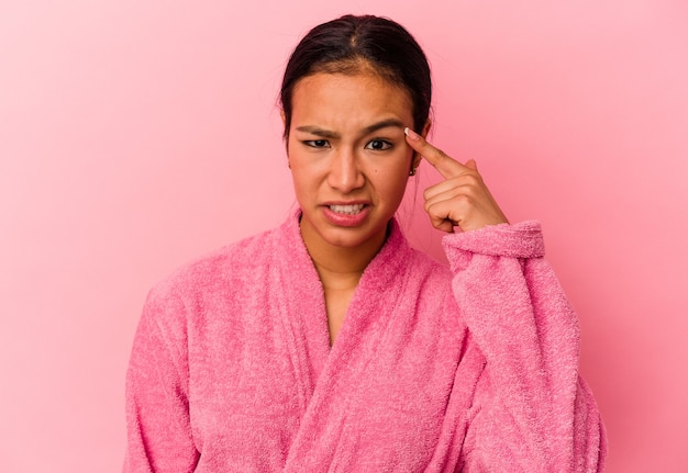 Young Venezuelan woman wearing a bathrobe isolated on pink background showing a disappointment gesture with forefinger.