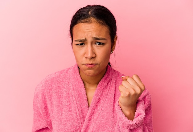 Young Venezuelan woman wearing a bathrobe isolated on pink background showing fist to camera aggressive facial expression