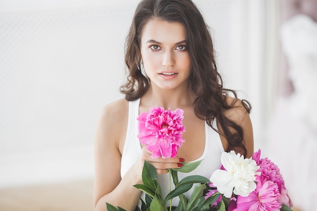 Young very beautiful woman with flowers indoors. Closeup portrait of attractive female.