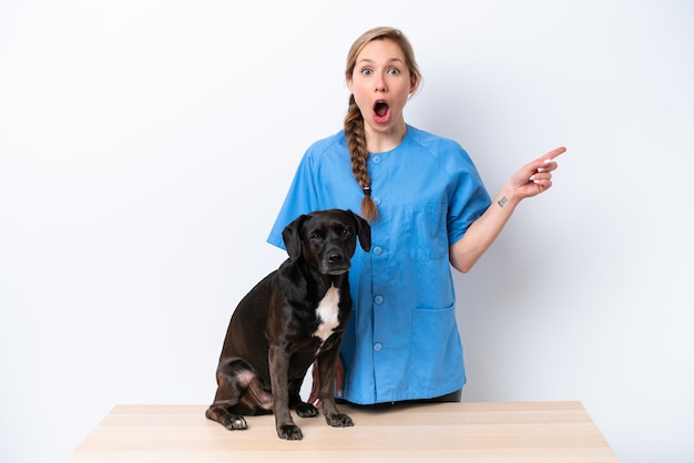 Young veterinarian woman with dog isolated on white background surprised and pointing finger to the side