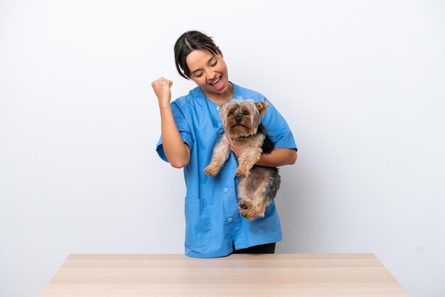 Young veterinarian woman with dog on a table isolated on white background celebrating a victory