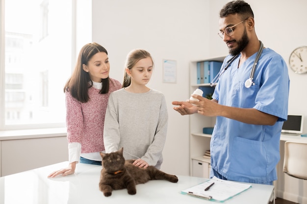 Giovane medico veterinario che mostra una medicina efficace per il gatto mentre consulta i proprietari dell'animale domestico nelle cliniche