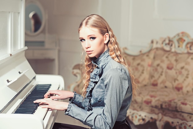 Young victorian girl in a tender blue dress learning to play
piano lovely blond with curly hair woman sitting in room with
vintage sofa private education concept