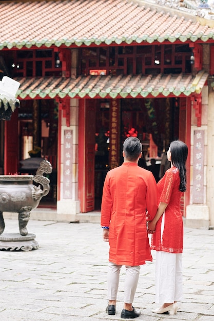 Young Vietnamese couple in traditional clothes looking at old temple when walking outdoors on Lunar New Year