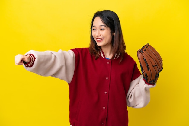 Молодая вьетнамская женщина-игрок в бейсбольной перчатке на желтом фоне показывает большой палец вверх