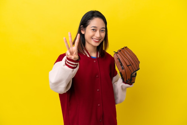 Young Vietnamese player woman with baseball glove isolated on yellow background happy and counting three with fingers